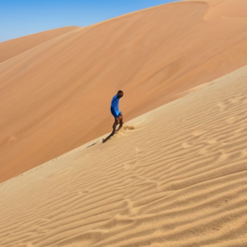 **Sand Surfing Experience**: Create an image of a person standing on top of a large sand dune in Botswana, looking down with excitement. The scene should capture the vast desert landscape with a blue sky, highlighting the thrill of sand surfing.